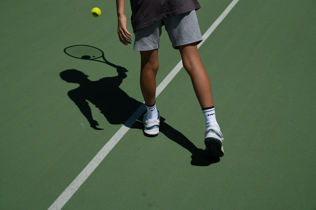 Why do tennis players wear long socks? Tennis player bouncing ball with tennis socks.