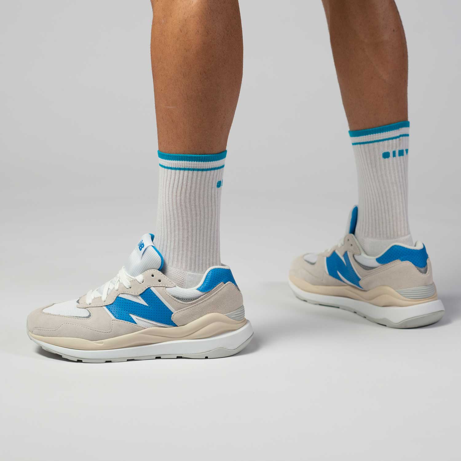 Clay Active's white and blue men's tennis socks in studio with New Balance shoes.